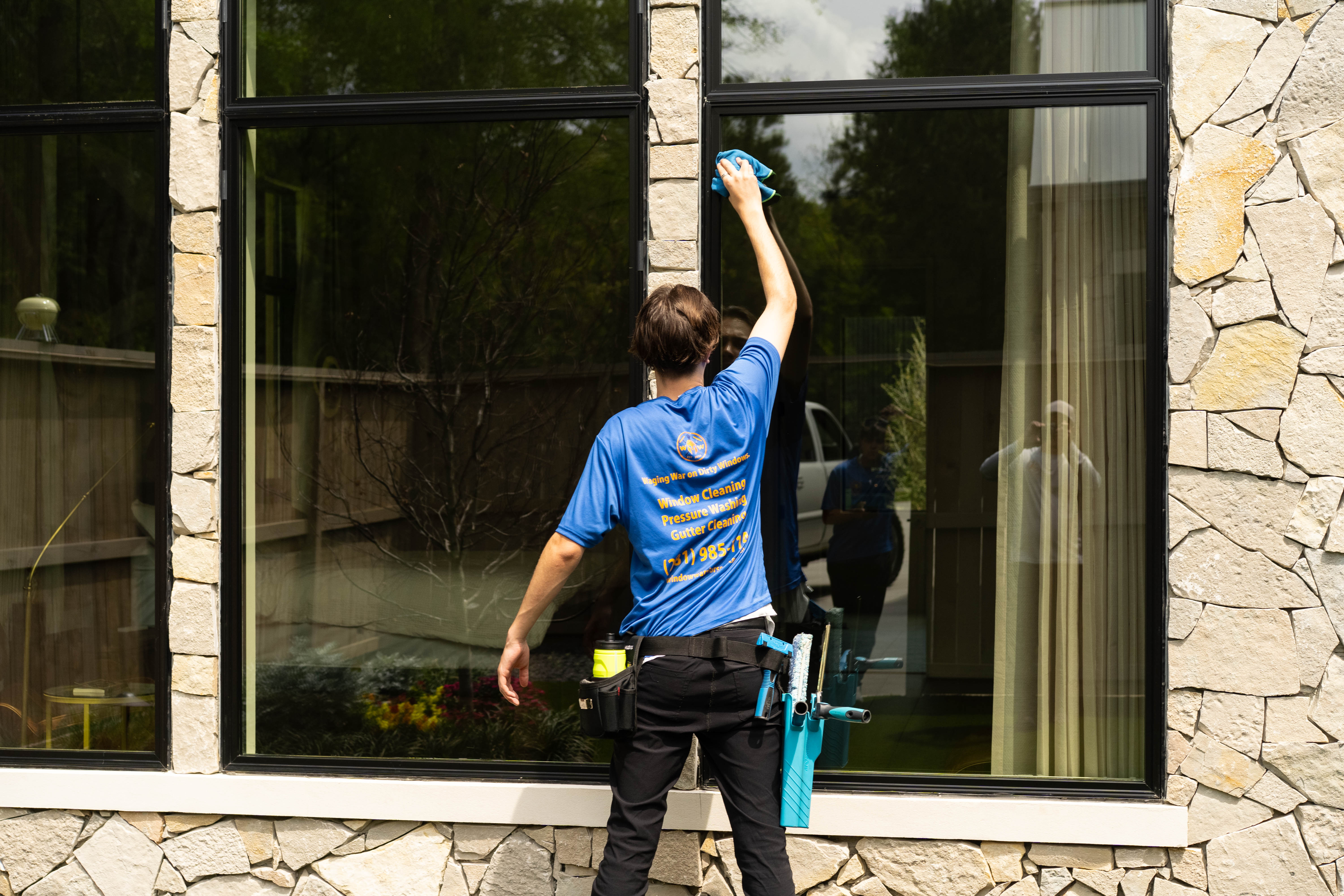 Window Warriors technician cleaning exterior windows on a stone Houston home