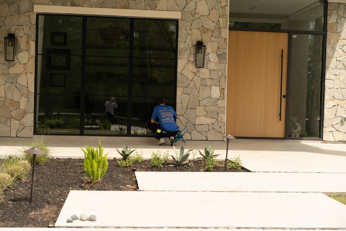 Window Warriors technician cleaning floor-to-ceiling windows on a stone modern home