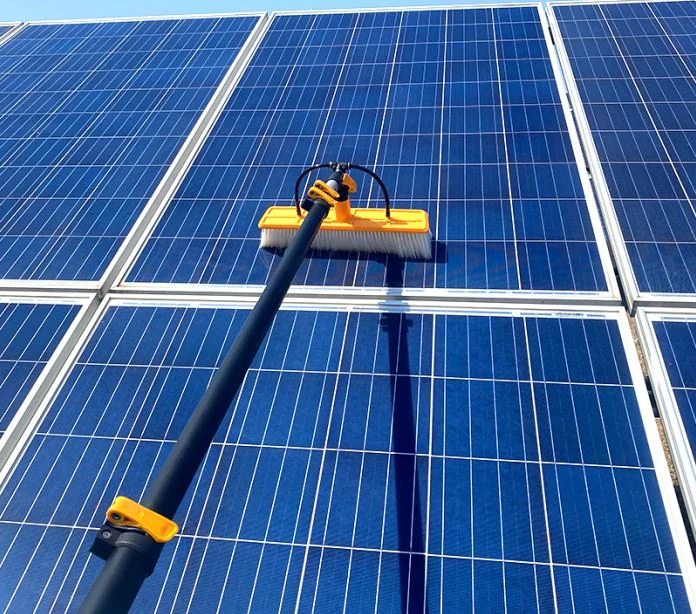 Technician using a soft-bristle brush to clean a residential solar panel array