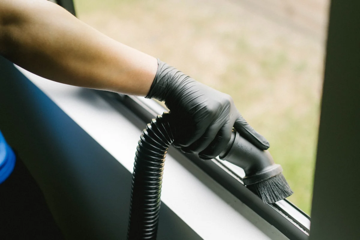 Technician hand-detailing a window track with a brush and vacuum tool