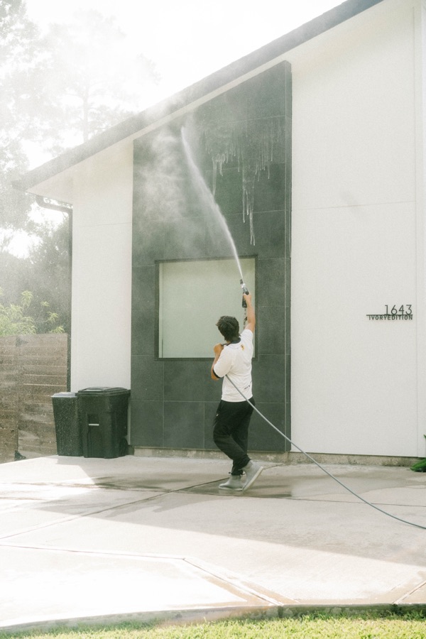 Pressure washing exterior siding on a modern white Houston home